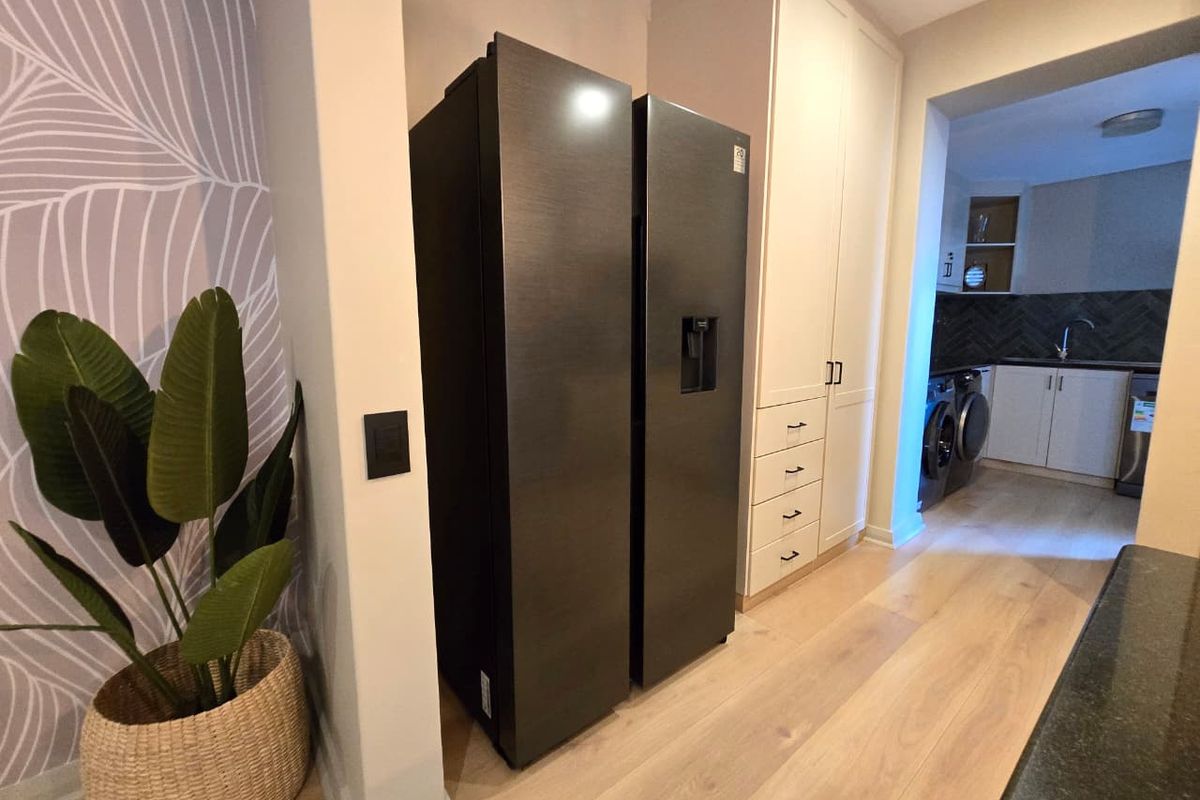 Modern kitchen area featuring built-in cabinetry, light wood-look flooring, and a tiled backsplash, leading into a functional scullery or laundry space.