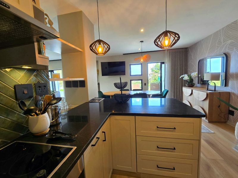Modern open-plan kitchen and living area featuring a central island with granite countertops, shaker cabinetry, and stylish pendant lighting, flowing into a bright dining space.