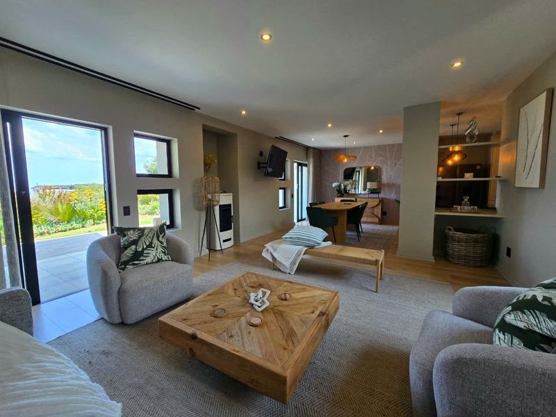 Spacious open-plan living and dining area featuring modern recessed lighting, a sleek fireplace, and large sliding doors opening to an outdoor patio.