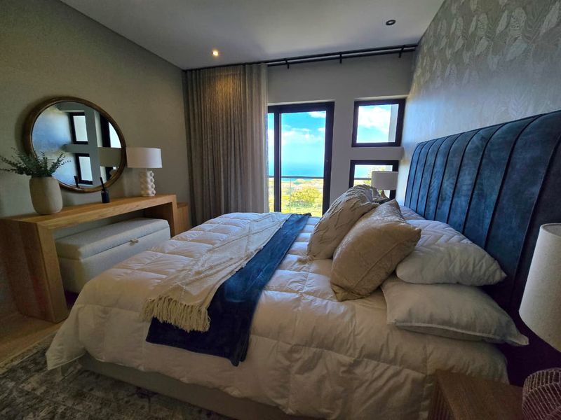 A well-appointed bedroom featuring modern recessed lighting, textured wallpaper, and a sliding glass door providing access to a balcony with scenic views.