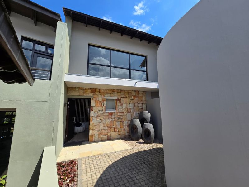 Front entrance of the apartment featuring stone cladding, a paved walkway, and large windows under a tiled roof.