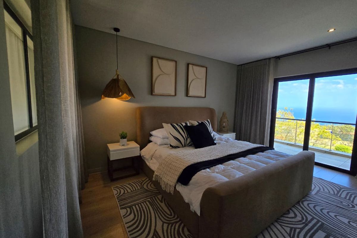 A well-appointed bedroom featuring modern recessed lighting, laminate flooring, and a large sliding glass door providing access to a balcony with scenic views.