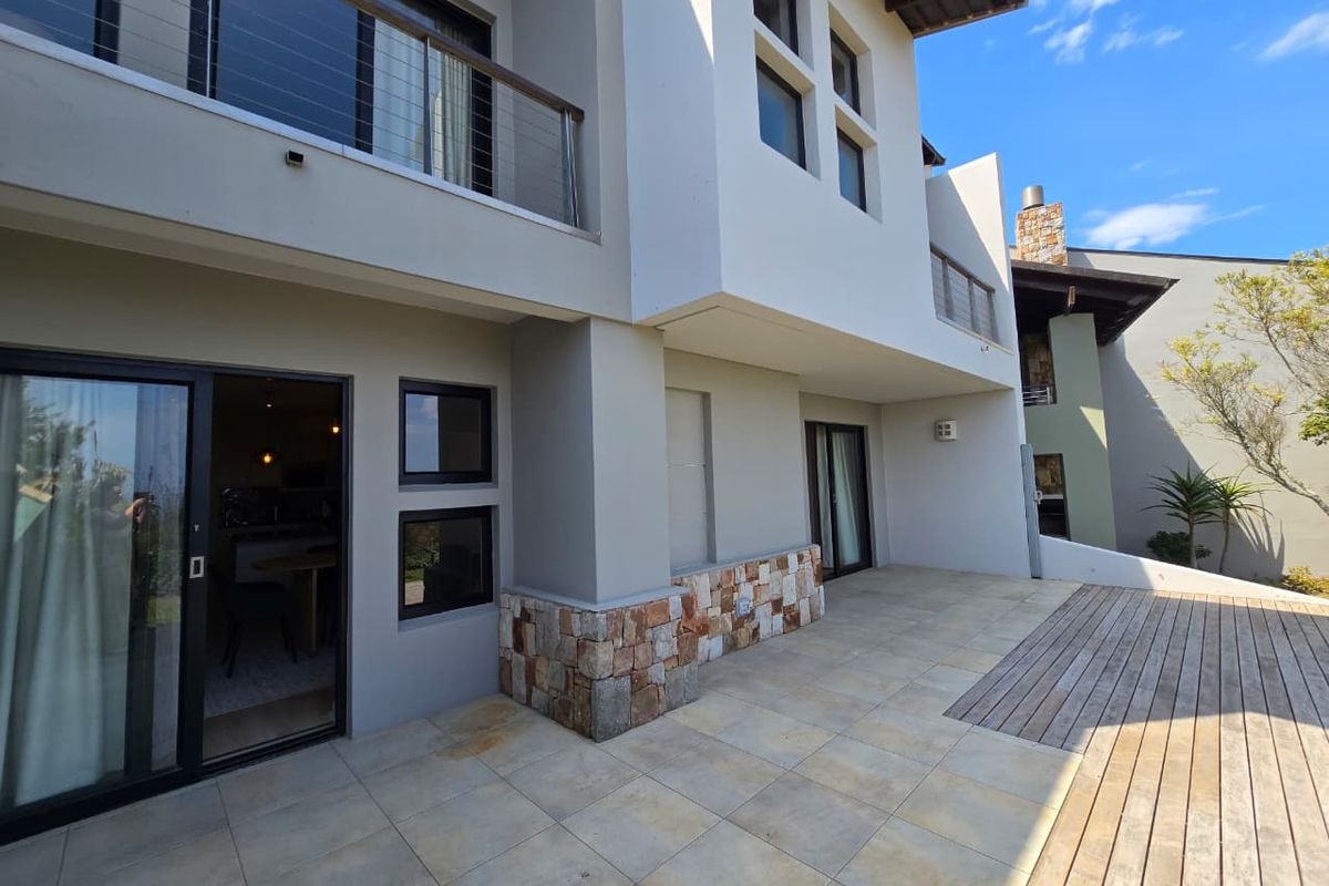 A spacious rear patio featuring a combination of tiled flooring and timber decking, stone-clad accents, and direct access to the interior via sliding glass doors.
