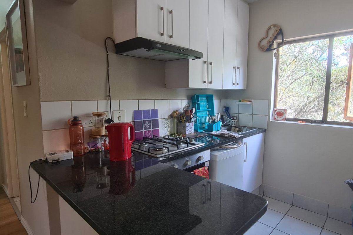 Compact kitchen featuring granite countertops, gas hob, extractor fan, and white cabinetry with tiled backsplash and flooring.