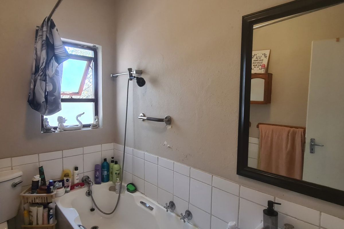 A functional bathroom featuring a bathtub with shower mixer, tiled splashback, toilet, and a wall-mounted mirror, requiring some cosmetic wall repairs.