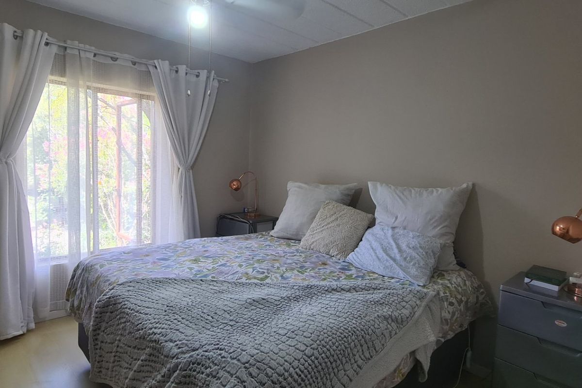A bedroom featuring a ceiling fan and a window with curtains, providing natural light and ventilation.