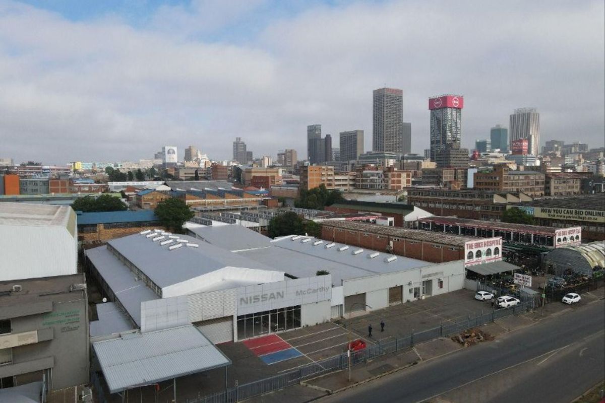 Aerial view of an industrial property featuring a large warehouse facility with metal roofing, skylights, and a paved parking area in an urban setting.