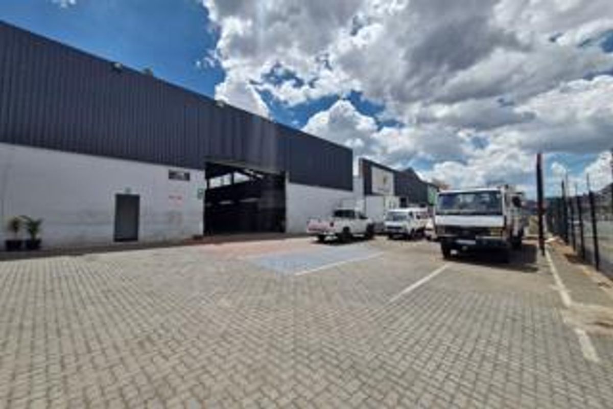 Industrial property exterior featuring a large roller shutter door, paved yard area, and metal cladding facade.