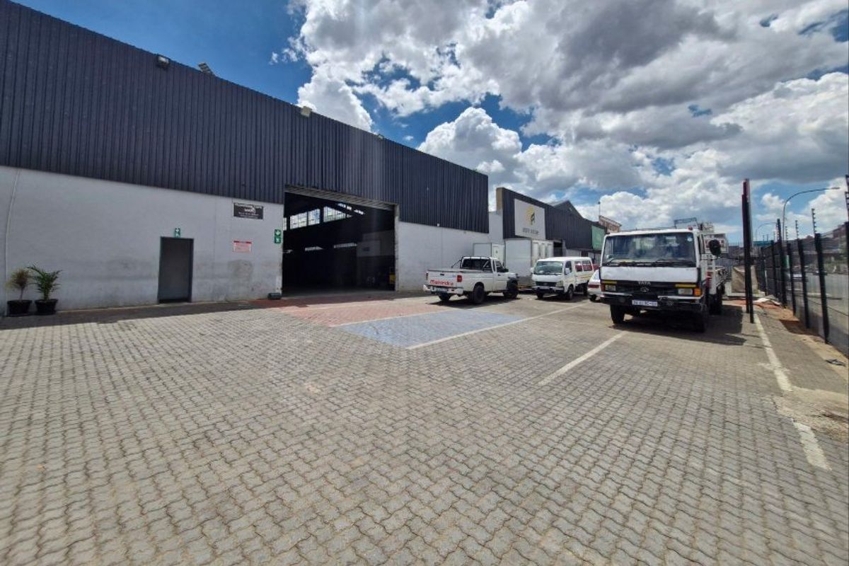 Industrial property exterior featuring a paved driveway, large roller shutter access, and metal cladding facade.