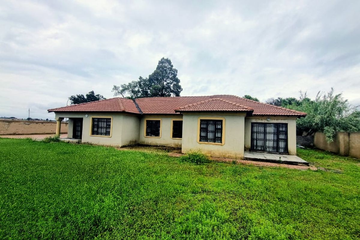 Rear view of a single-story house featuring a tiled roof, security bars on windows, and a large surrounding lawn with boundary walls.