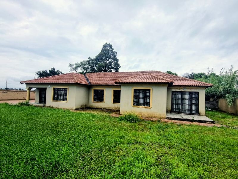 Rear view of a single-story house featuring a tiled roof, security bars on windows, and a large surrounding lawn with boundary walls.