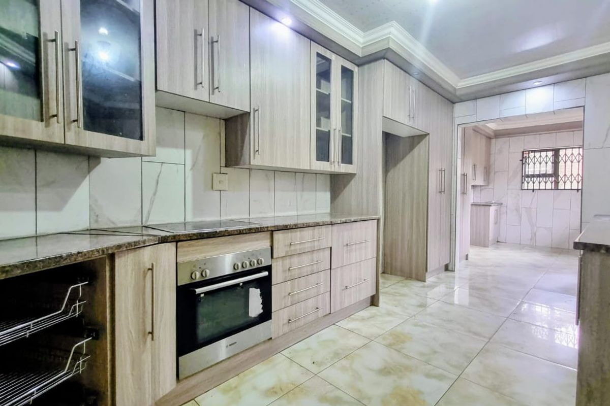 Modern kitchen featuring light wood-grain cabinetry, granite countertops, built-in oven, hob, and tiled finishes, with an adjoining scullery area.