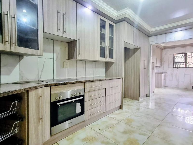 Modern kitchen featuring light wood-grain cabinetry, granite countertops, built-in oven, hob, and tiled finishes, with an adjoining scullery area.