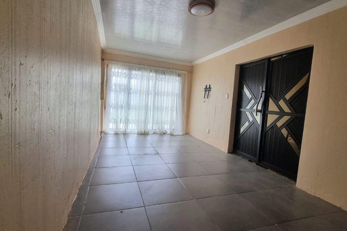 An empty living area featuring tiled flooring, ceiling coving, and a secure entrance door, offering a blank canvas for interior design.