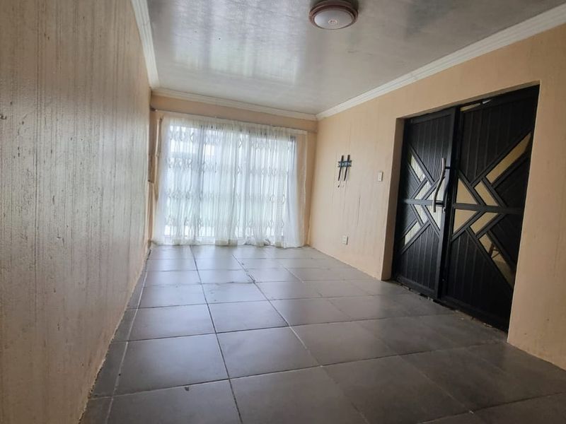An empty living area featuring tiled flooring, ceiling coving, and a secure entrance door, offering a blank canvas for interior design.