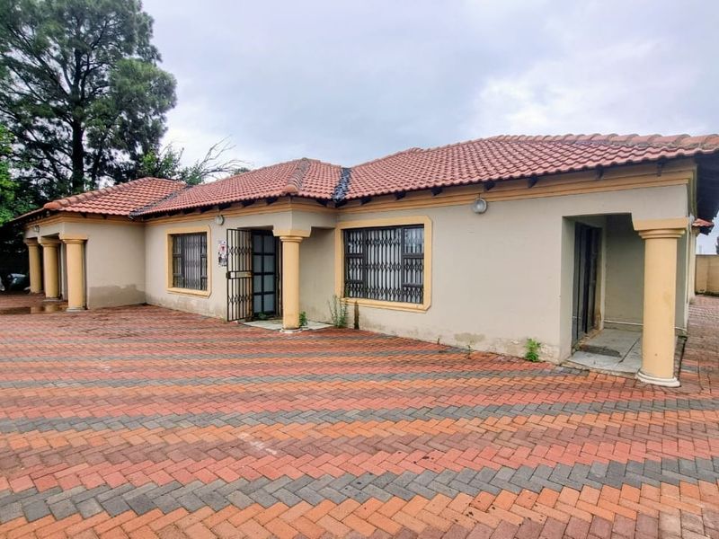 Front elevation of a single-story house featuring a terracotta tiled roof, decorative columns, and an extensive paved driveway area.