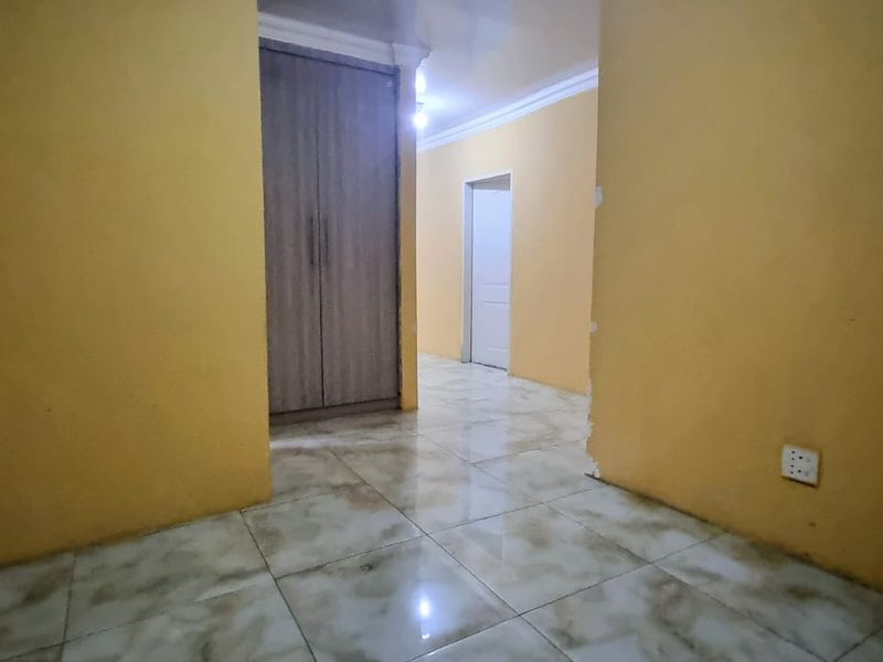 An empty bedroom featuring tiled flooring, a built-in wardrobe, and yellow painted walls with some visible wear near the doorway.