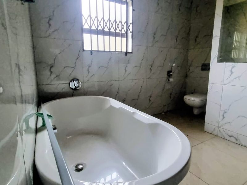 A functional bathroom featuring a bathtub, toilet, and marble-look wall tiles with security bars on the window.