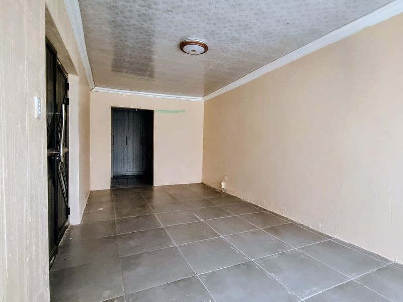 An empty living area featuring tiled flooring, a ceiling light fixture, and a built-in cupboard, providing a blank canvas for interior design.