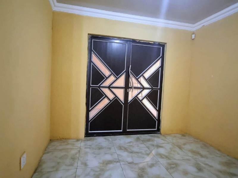 An empty living room featuring tiled flooring, crown molding, and a decorative double door entrance.