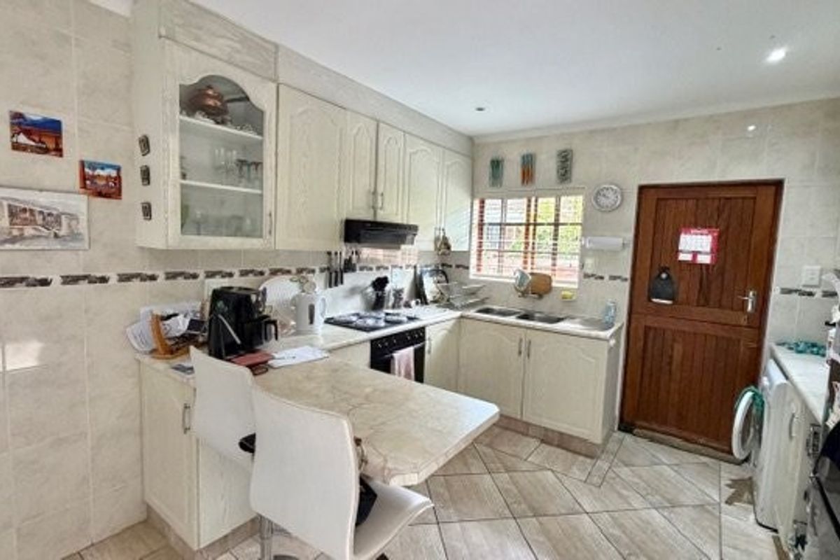 A functional kitchen featuring built-in cabinetry, laminate countertops, a double basin sink, and tiled finishes throughout, providing a practical workspace.