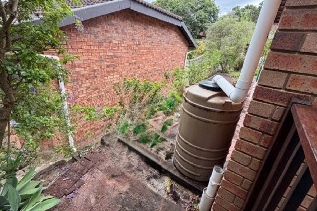Rear exterior view of the townhouse featuring a brick facade, a rainwater collection tank, and a sloped garden area with a retaining wall.