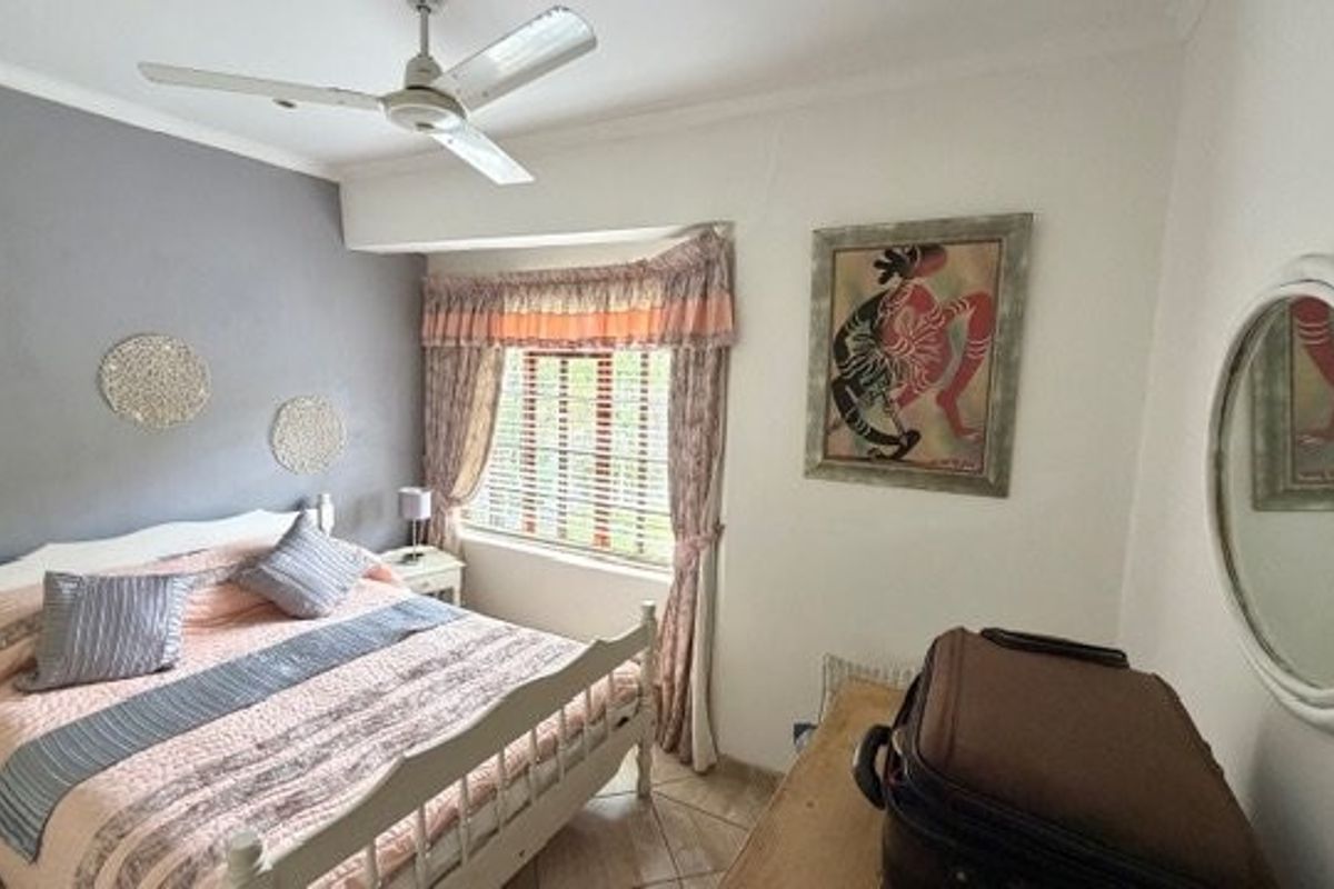 A bedroom featuring tiled flooring, a ceiling fan, and window blinds, providing a functional space with neutral wall finishes.
