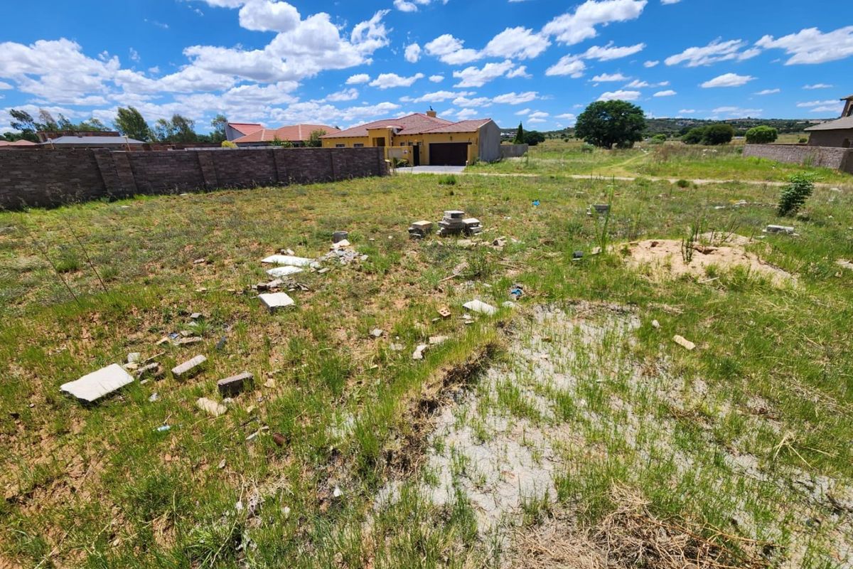 A vacant residential plot featuring natural grass cover and a perimeter boundary wall, offering a clear space for future development.