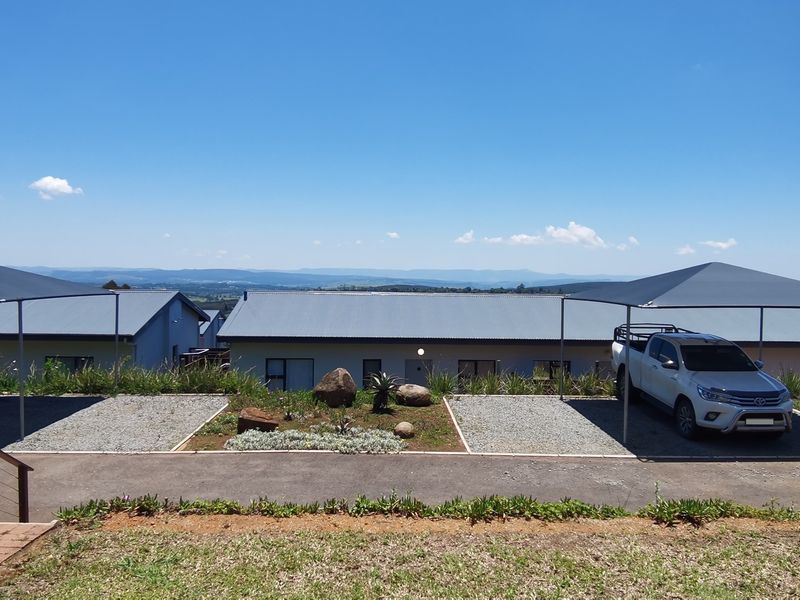Front exterior view of the townhouse complex featuring covered parking bays, gravel driveways, and landscaped garden beds with scenic mountain views.