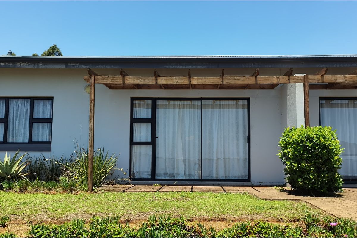 Rear exterior view of the townhouse featuring a paved patio area, timber pergola, and sliding glass doors leading into the living space.