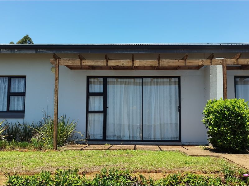 Rear exterior view of the townhouse featuring a paved patio area, timber pergola, and sliding glass doors leading into the living space.