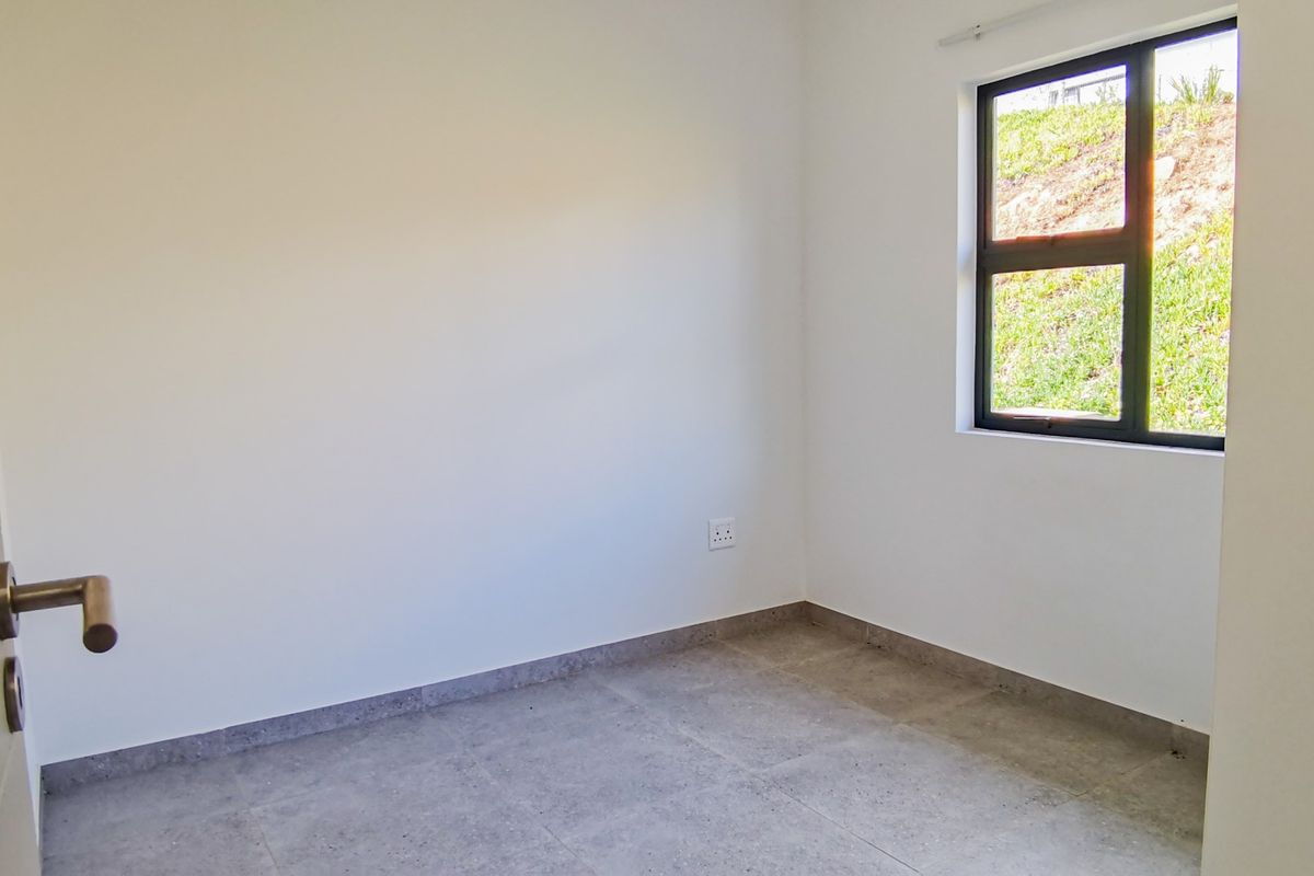 A clean, empty bedroom featuring neutral tiled flooring, white walls, and a modern aluminium-framed window providing natural light.