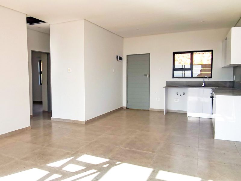 An open-plan living and kitchen area featuring neutral tiled flooring, modern white cabinetry, and clean finishes in a bright, vacant space.