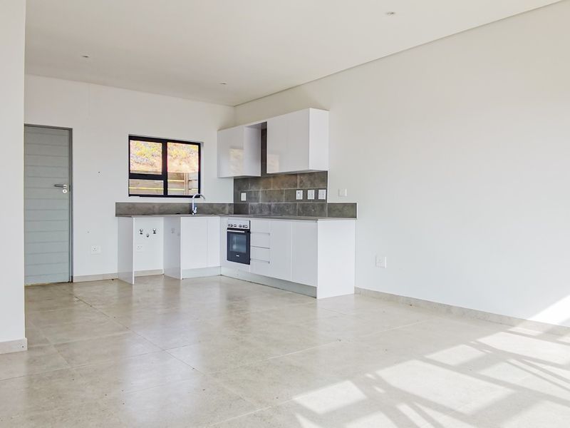 Modern open-plan kitchen featuring white cabinetry, built-in oven, hob, and neutral tiled flooring in a bright, spacious living area.