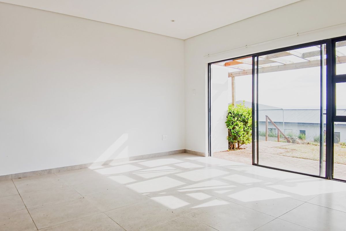 A bright, empty living room featuring large sliding glass doors that open onto an outdoor patio area with tiled flooring throughout.