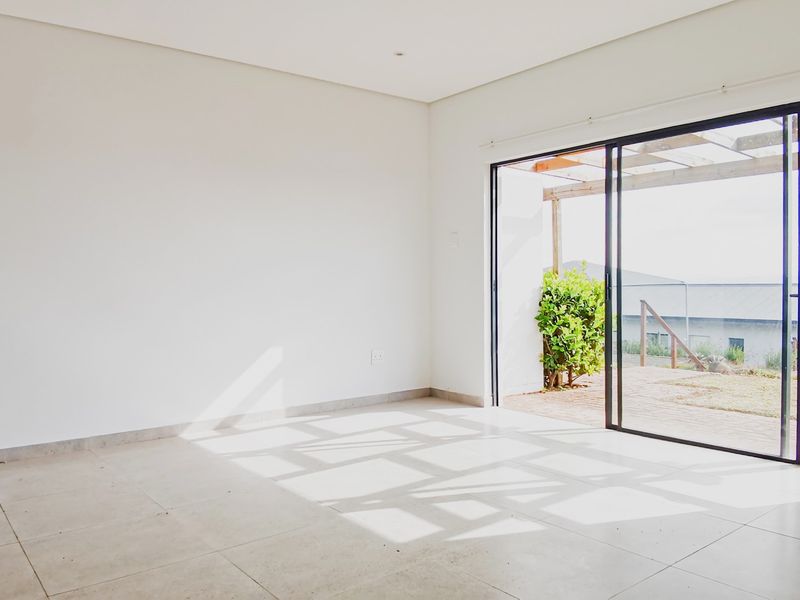 A bright, empty living room featuring large sliding glass doors that open onto an outdoor patio area with tiled flooring throughout.