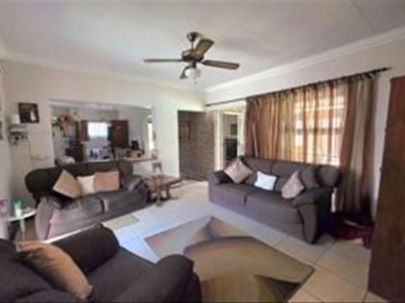 A spacious living room featuring tiled flooring, a ceiling fan, and coved cornicing, with an open-plan flow leading into the adjacent kitchen area.