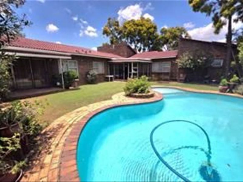 A rear view of the property featuring a swimming pool with brick paving, a landscaped garden, and a brick-built house with a tiled roof.