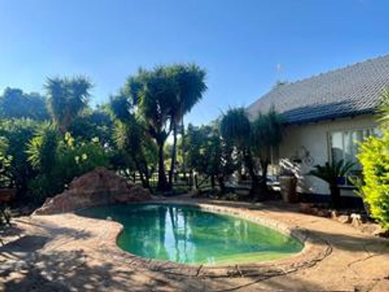 Outdoor pool area featuring a natural rock water feature, paved surround, and established garden landscaping adjacent to the main dwelling.
