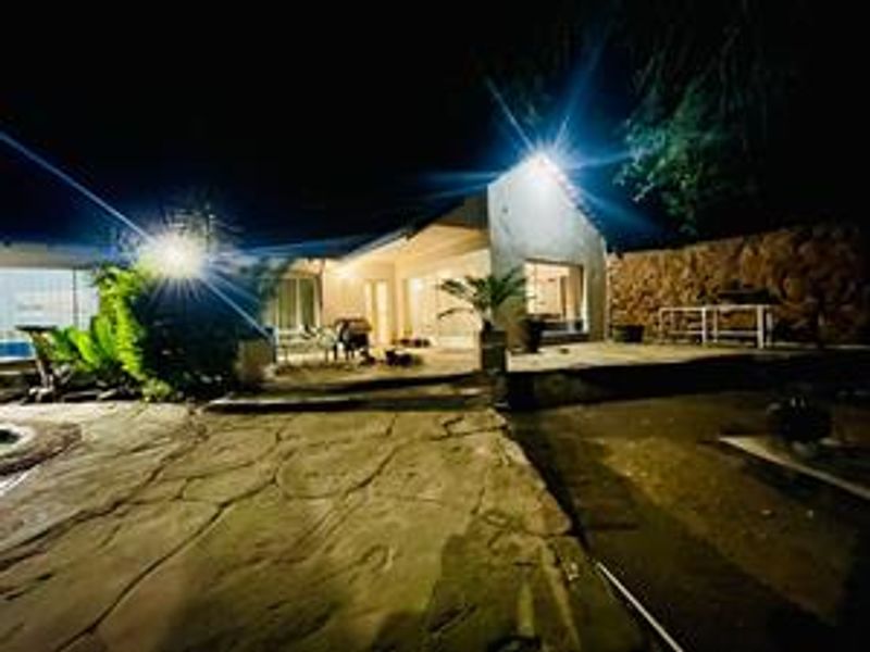 Night view of the rear exterior featuring a stone paved patio area, swimming pool, and stone retaining wall.