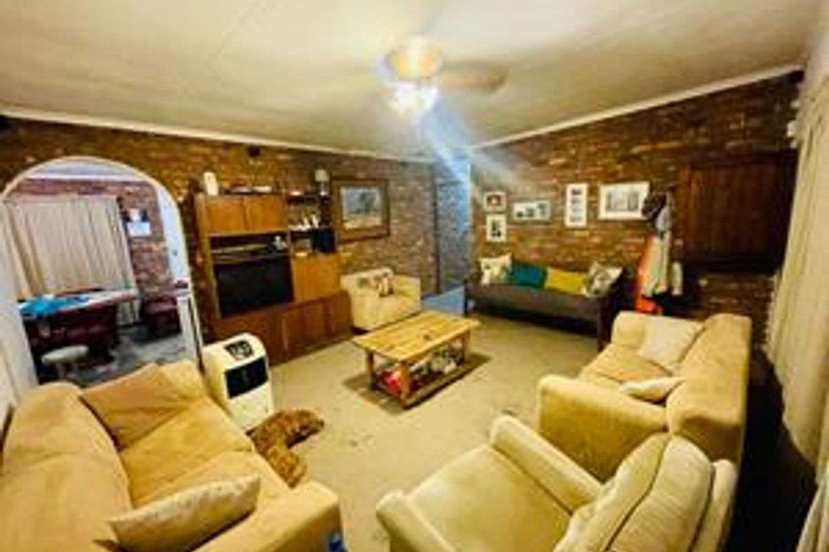 A spacious living room featuring exposed brick walls and a ceiling fan, offering a rustic aesthetic with potential for modern updates.