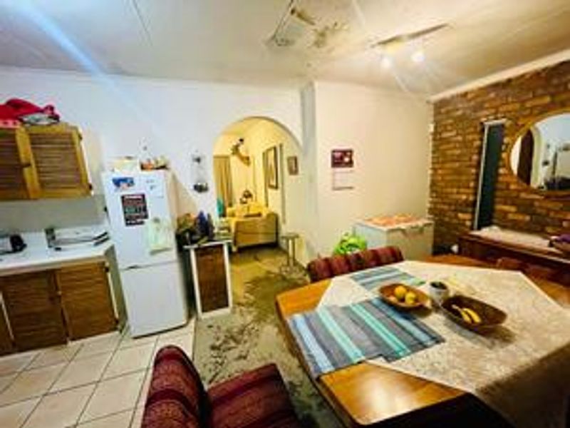 Open-plan kitchen and dining area featuring exposed brickwork, an arched transition, and tiled flooring, currently showing signs of ceiling water damage and floor staining.