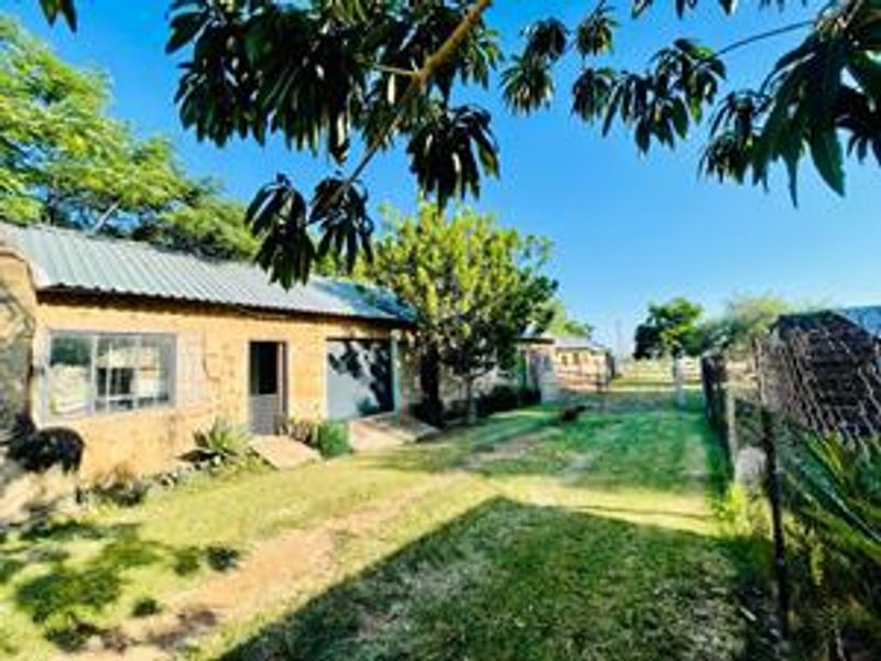 Rear view of a farm building featuring stone masonry walls and a corrugated metal roof, set within a spacious garden area with perimeter fencing.
