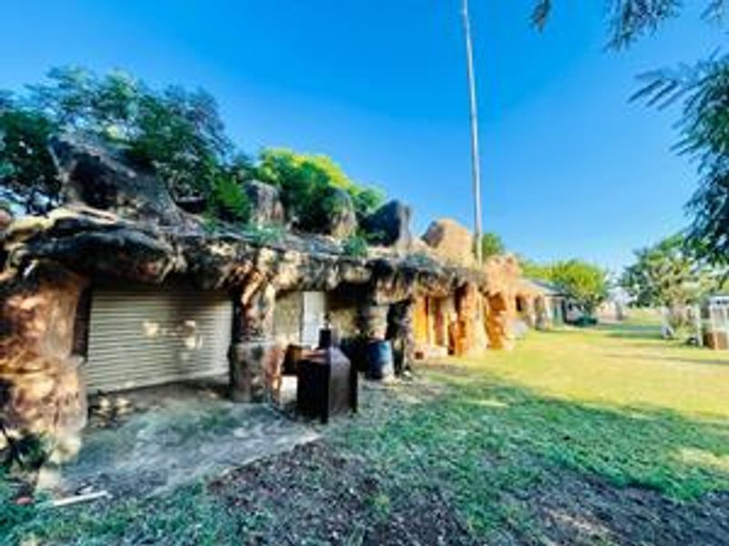Rear view of a farm property featuring a unique rock-faced exterior facade and a roller shutter door opening onto a concrete patio area.