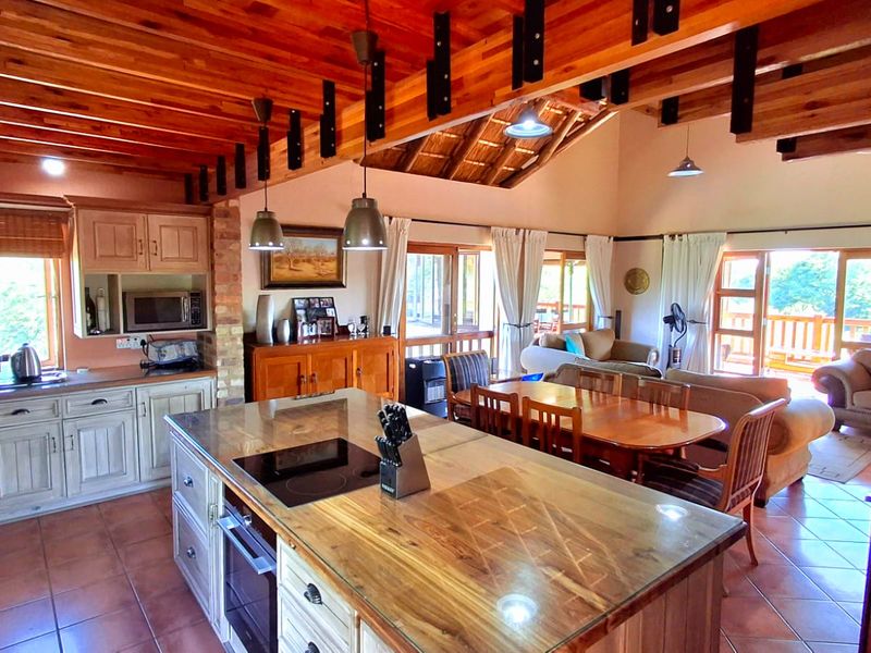 Spacious open-plan living area featuring a kitchen with a central island, exposed timber beams, vaulted ceilings, and direct access to an outdoor deck.