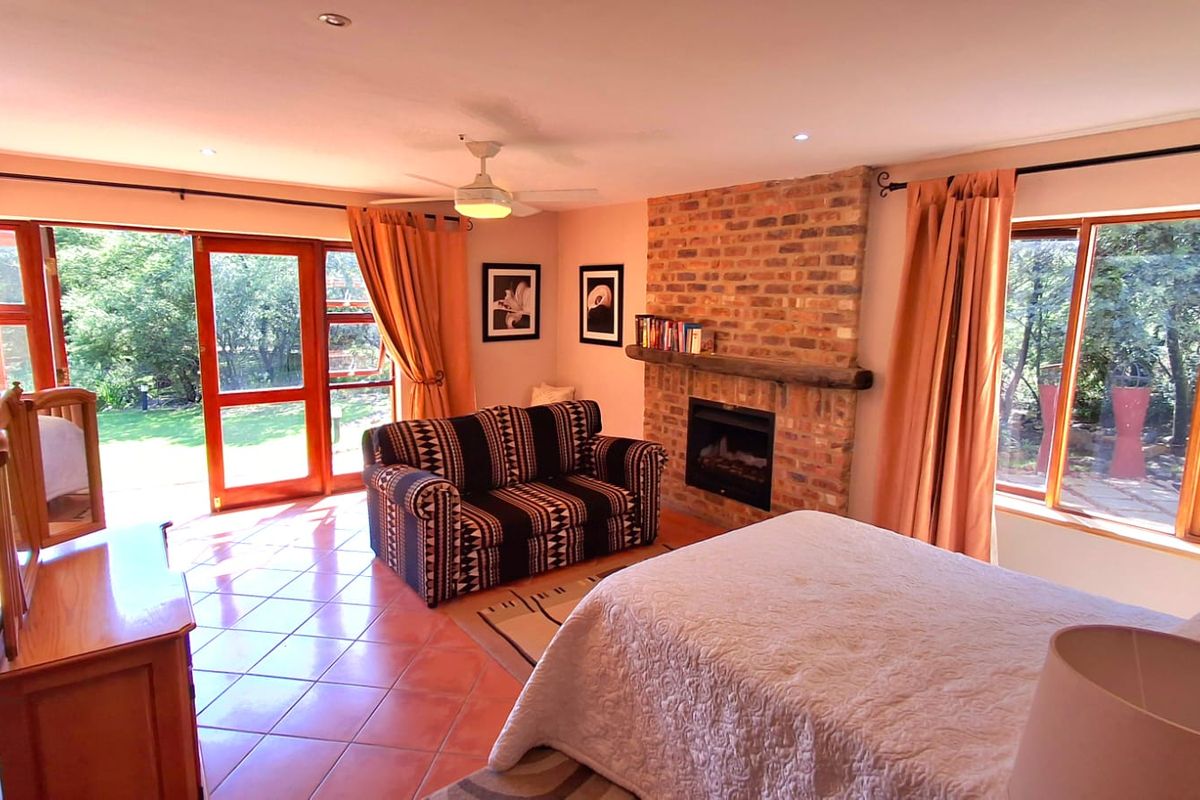 Spacious bedroom featuring a rustic brick fireplace, timber mantelpiece, tiled flooring, and large timber-framed glass doors providing direct access to the garden.