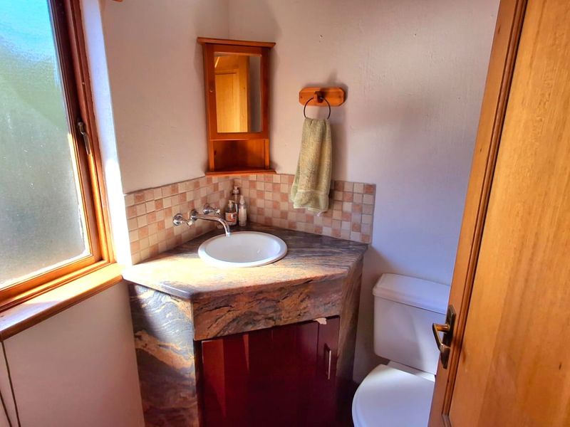 Compact bathroom featuring a corner vanity with stone countertop, drop-in basin, wall-mounted tap, and a matching corner medicine cabinet.
