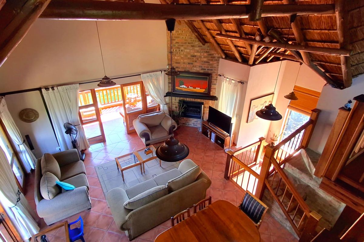 Spacious open-plan living area featuring a high vaulted thatch ceiling with exposed timber rafters, a brick fireplace, and direct access to an outdoor balcony.