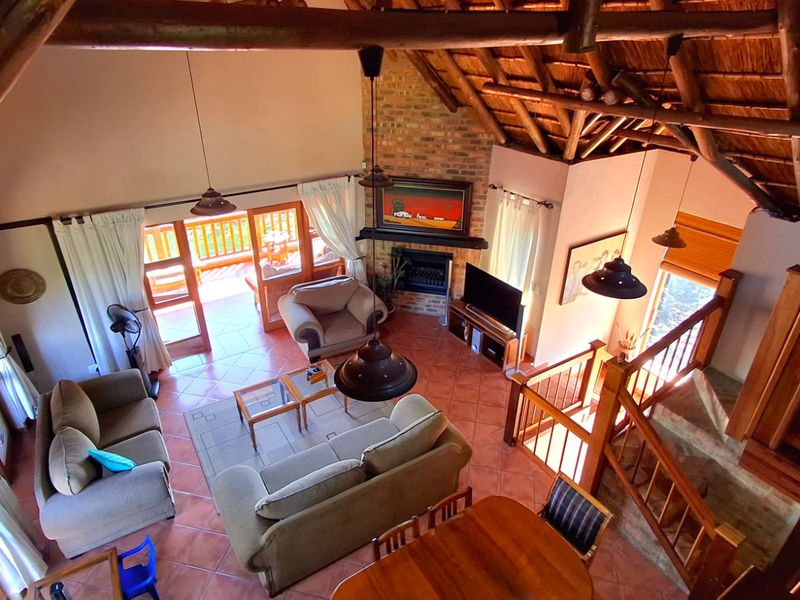 Spacious open-plan living area featuring a high vaulted thatch ceiling with exposed timber rafters, a brick fireplace, and direct access to an outdoor balcony.