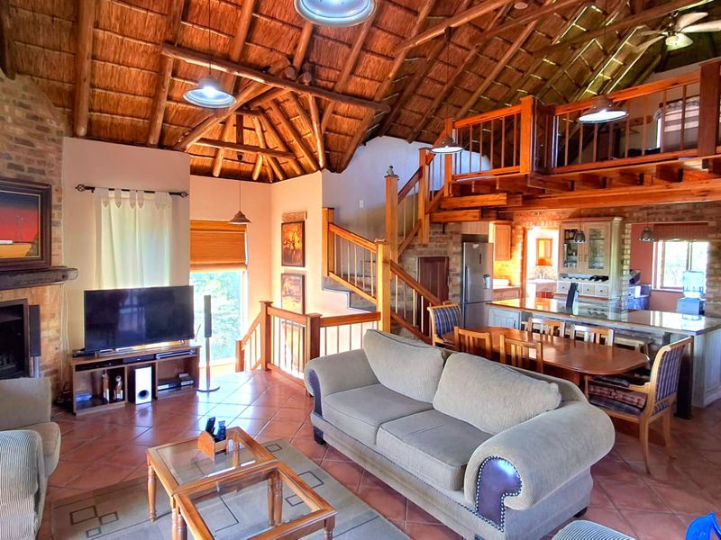 Spacious open-plan living area featuring a high thatched ceiling with exposed timber trusses, a brick fireplace, and a mezzanine level with timber staircase.